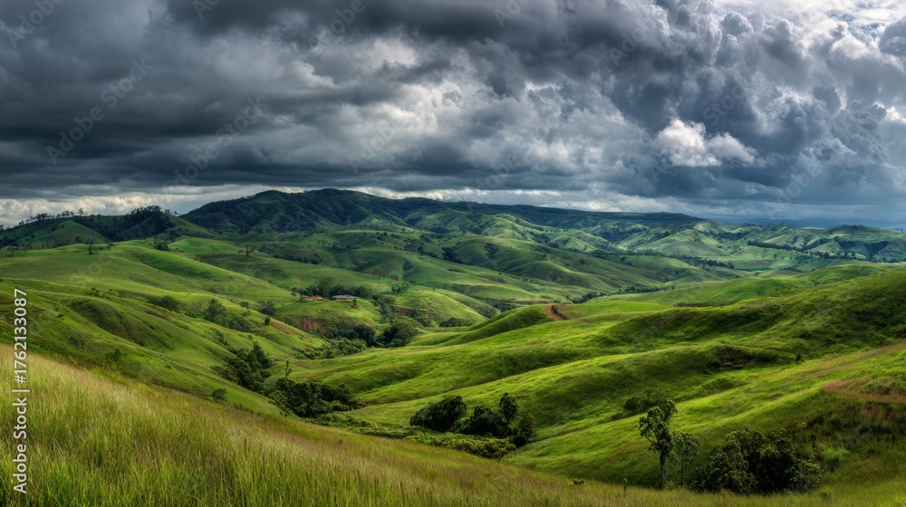 Obraz premium Rolling green hills create a peaceful scene with dark clouds brooding above in the distance.