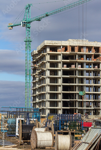 High-rise residential building under construction with multiple green tower cranes operating at the site. Industrial urban development scene ideal for illustrating architecture, engineering, and const