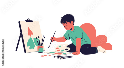 A young boy is painting on the floor with an easel and brushes in a bright room space