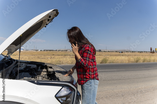 Valokuva woman is talking on phone while looking at her car's engine with the hood open