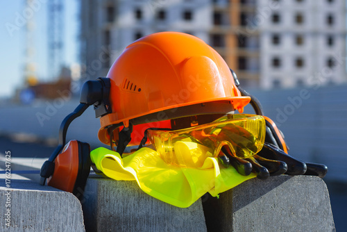Φωτογραφία Construction safety equipment including a hard hat, protective gloves with goggles and ear defenders lies on a construction site