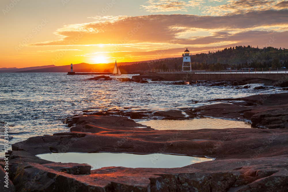 Fototapeta premium Sailboat entering the harbor at Grand Marais viewed from Artist's Point at sunset on an autumn day