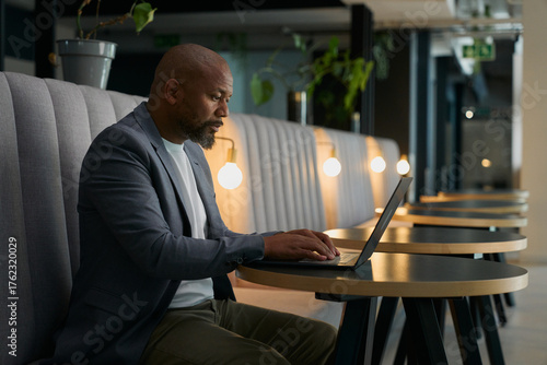 Side view of focused mature businessman in blazer using laptop at desk in office lounge