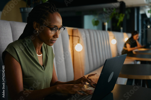 Focused young black businesswoman typing on laptop sitting at desk in office lounge