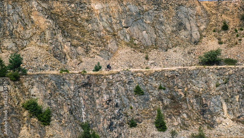 Warstwowy krajobraz kamieniołomu ze skalistymi klifami i rozproszonymi zielonymi drzewami pod zachmurzonym niebem 