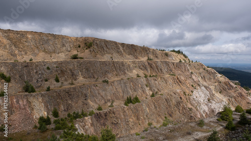 Warstwowy krajobraz kamieniołomu ze skalistymi klifami i rozproszonymi zielonymi drzewami pod zachmurzonym niebem 