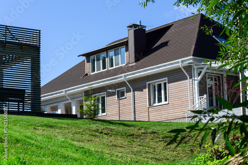 Residential house with porch lawn and wooden structures under clear blue sky. Well maintained countryside home with porch carport and wooden annex ideal for real estate architecture lifestyle.
