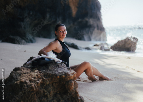 Smiling young woman in black surf suit relaxing on tropical beach in Bali, Indonesia