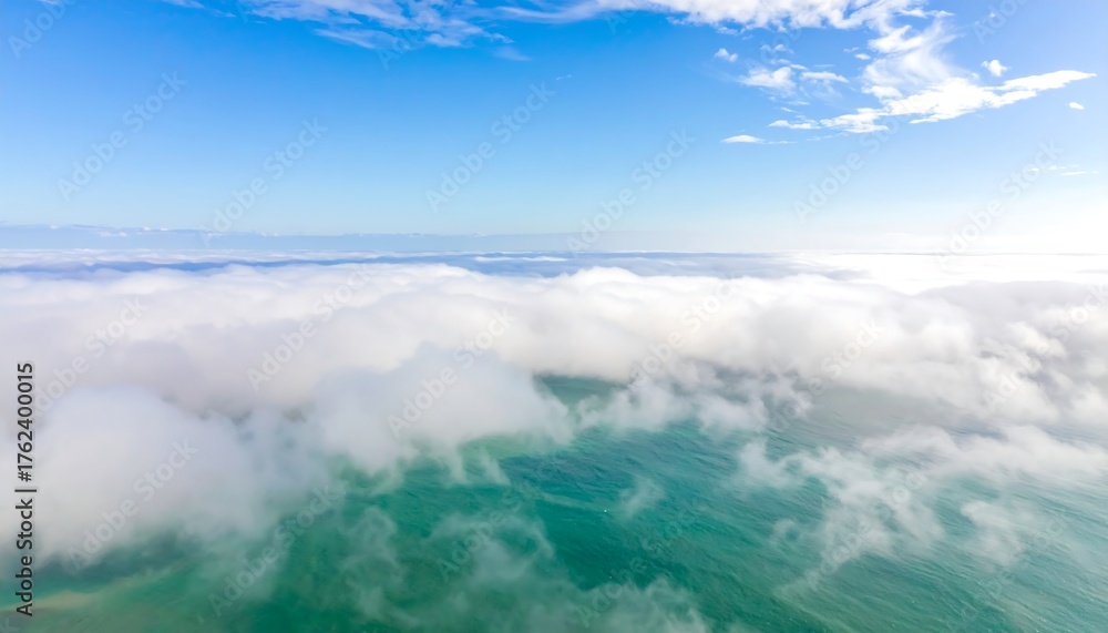 Obraz premium An aerial view capturing fluffy white clouds rolling over turquoise ocean water under a bright, clear, blue sky with soft haze