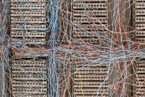 network hub, multi-colored copper wires crossing over white numbered cross-connect panels. The chaotic a a large old telephone telecommunications network.