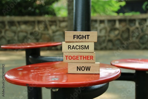 Φωτογραφία Bold wooden blocks spell out 'FIGHT RACISM TOGETHER NOW' on red park tables, promoting unity, inclusivity, and collective action against racism in a natural outdoor setting