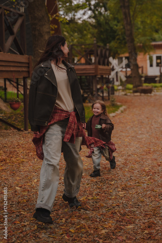 A little girl catches up with her mother on a walk in nature. A family bow for a walk outside the city. Mom and daughter play in the yard in the fall. Vertical photo. 