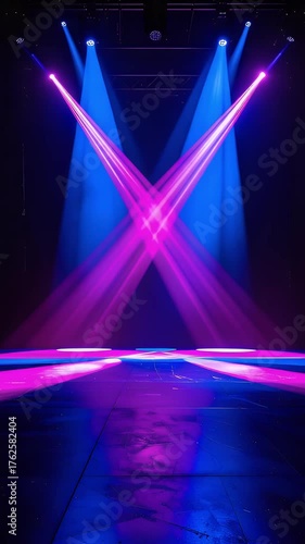 Vibrant purple and blue spotlights illuminate an empty stage with dynamic cross beams, creating an energetic background for performances or presentations.