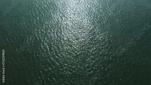Aerial drone video hovering high above the Atlantic Ocean. Calm deep-green water with sunlight reflections creating a peaceful, abstract marine texture. Ideal for travel, nature