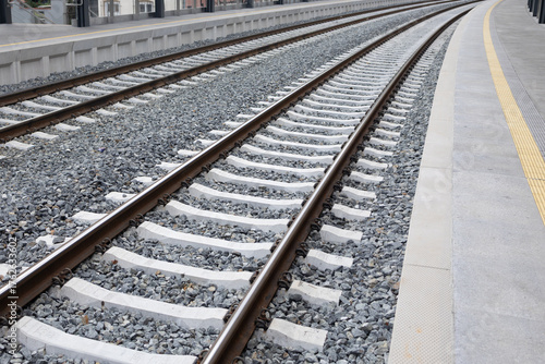 Railway tracks with gravel bed and concrete ties, curving gently along the platform, showcasing the infrastructure of modern transportation systems