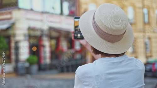 Young tourist girl in straw hat back view making video on phone capturing travel impressions about ancient old city on vacation