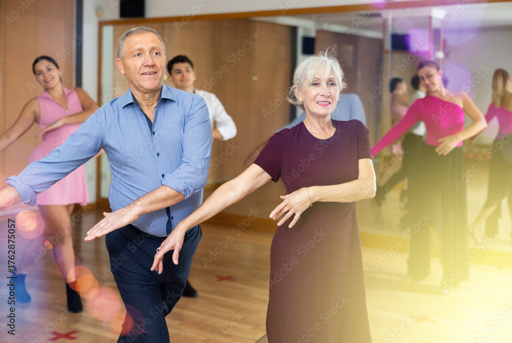 Obraz premium Cheerful elderly woman and man enjoying active dancing in pair during group training in dance studio, practicing playful jitterbug moves