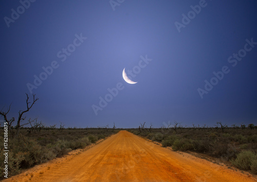 Desert road in outback Australia with moon in blue sky