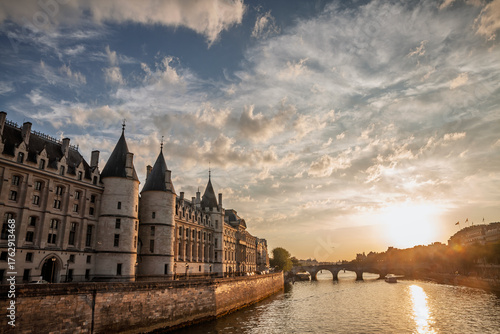 La Conciergerie along the Seine with Pont Neuf at dusk in Paris. The medieval palace and former prison stands by the river as the sun sets, a former prison is a major attraction on Ile de la Cité.