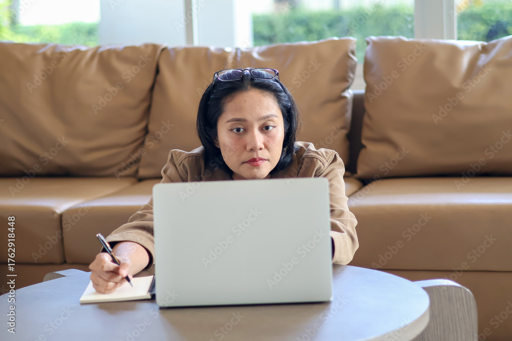 Naklejka premium Asian woman sitting on the floor with laptop on table taking notes in notebook, working from home, workspace