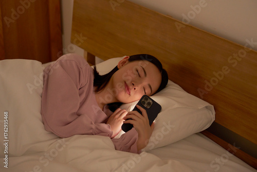 布団の中でスマホを使いながら寝落ちする女性