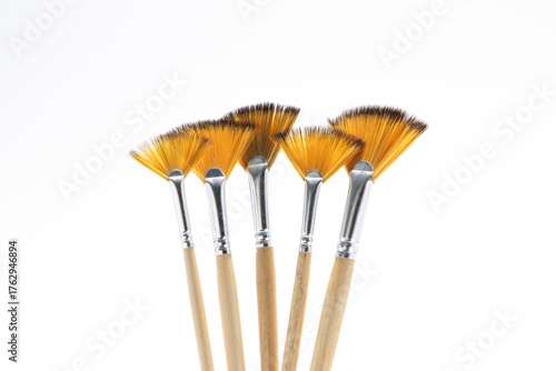 Fotografie A collection of fan paintbrushes with light wooden handles and amber synthetic bristles, isolated on a clean white background