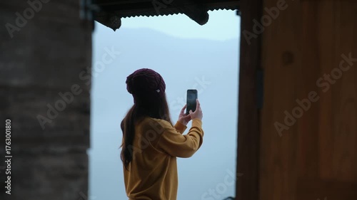 A woman using mobile phone to take photo of a beautiful view on foggy morning
