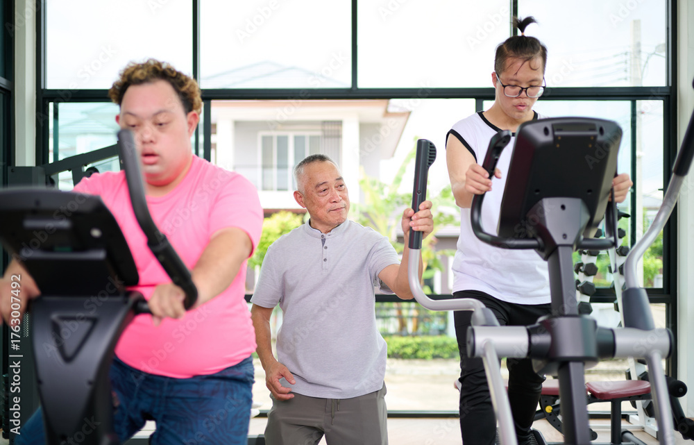Obraz premium A man with down syndrome exercising on an elliptical machine under the guidance of an elderly man at the gym