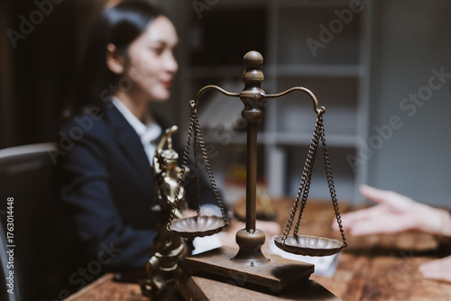 Female lawyer consulting client at desk with scales of justice, discussing legal documents, rights, and case strategy in office