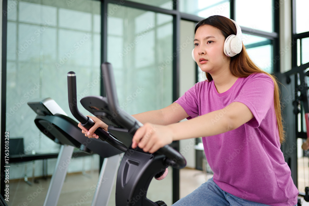 Obraz premium A woman exercising on a stationary bike while wearing headphones, indicating a focus on fitness and health