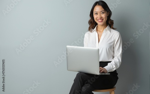Young business woman posing isolated over grey wall background sitting on stool using laptop computer. High quality