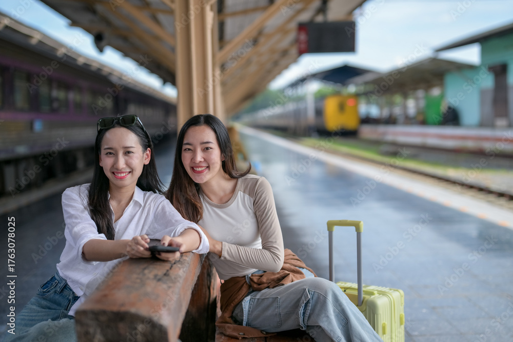 Fototapeta premium Two women sitting on a bench at a train station