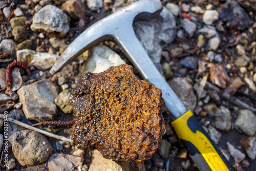 Wallpaper Mural A distinctively textured, rugged rock specimen lies on rocky ground next to a geological hammer. This unique, bumpy mineral evokes exploration and natural discovery Torontodigital.ca