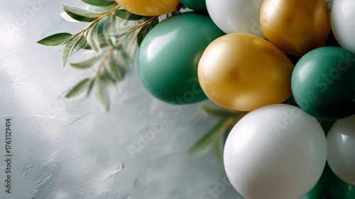 A close-up of decorative balloons in green, white, and gold, complemented by lush green leaves against a textured, light background.