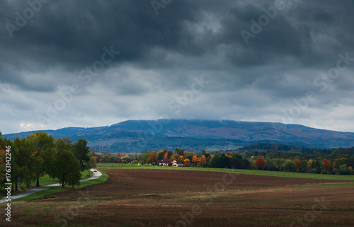 Small Czech village with autumn foliage trees under storm dramatic sky. Nature, landscape background