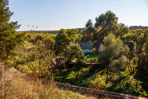 Quadro su tela A quaint little house nestled amidst lush green trees and sunlit foliage, offeri