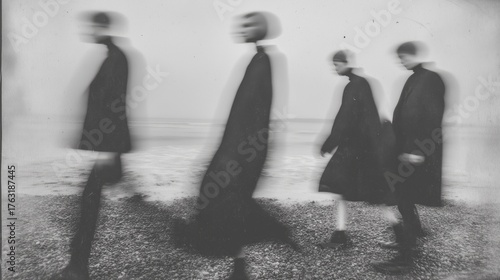 Abstract black and white image of blurred figures walking on a pebble beach, creating a surreal, dreamlike effect.