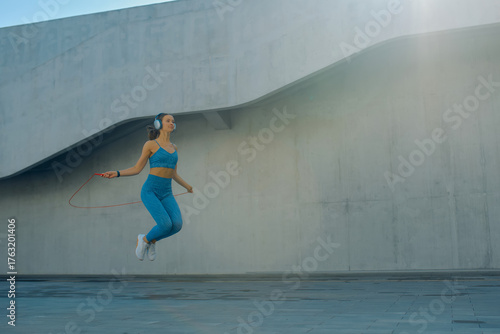 Woman jumps rope in a modern outdoor setting with clear sky and urban architecture