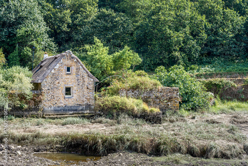 Old stone cottage by the Goyen river with stone wall and lush green forest surroundings, in the village of Pont-Croix in the Finistere department, in Brittany, France