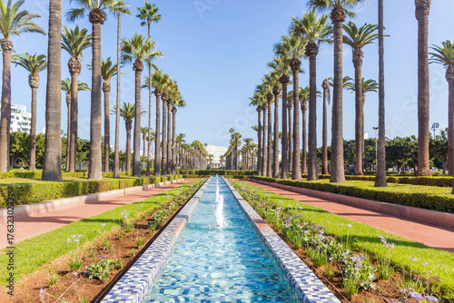 Palm trees and mosaic fountain in Arab League Park, Casablanca, Morocco. Urban garden with water channel and blue sky.