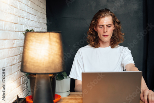 Young man working on laptop at a cozy desk with warm lighting in a modern space
