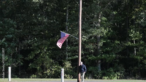 Leonardtown, Maryland USA A man walks on a large field beneath an American flag flying from a telephone pole.  