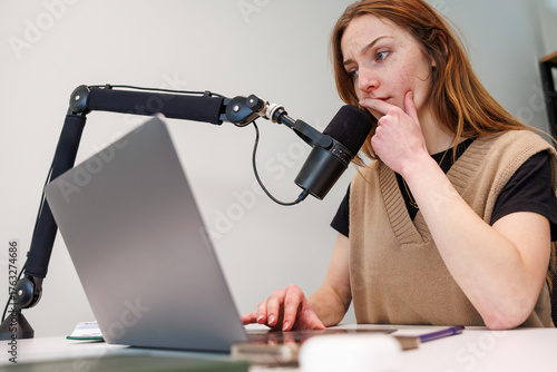 Cuadro en lienzo A young woman sits at a desk, speaks into a black dynamic mic on a boom arm, uses a laptop, with tablet, notebook, and earbuds case nearby, soft light, shallow depth