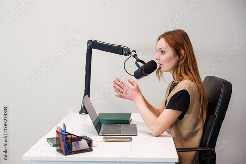 Fotografía Woman speaks into a condenser mic on boom arm at a white desk, gesturing as she