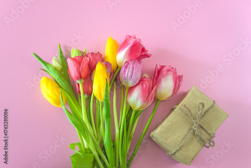 Bouquet of pink and yellow tulips flowers and craft gift box on a pink background. Spring holiday greeting card