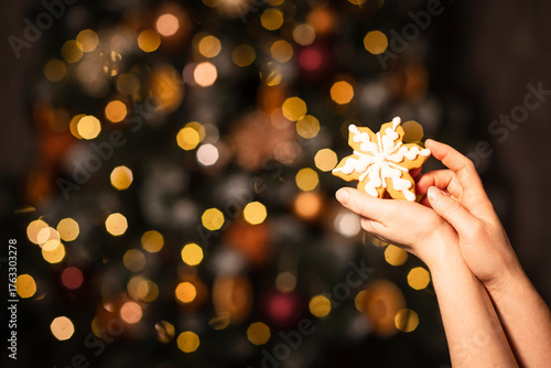 Gingerbread snowflake in female hands on Christmas background among New Year lights
