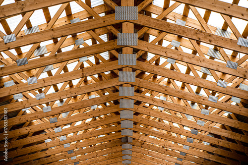 Symmetrical view of wooden roof trusses with metal plates in a modern building under construction. Abstract architectural pattern with repeating wooden beams and geometric structure.
