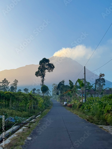 village road with view of active volcano emitting smoke in the morning