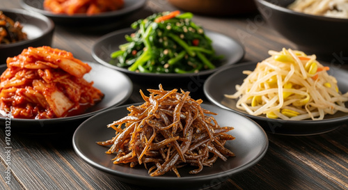 Assortment of classic Korean side dishes (banchan): spicy kimchi, seasoned spinach, stir-fried anchovies (myeolchi bokkeum), and soybean sprouts (kongnamul). Authentic Asian food table setting.