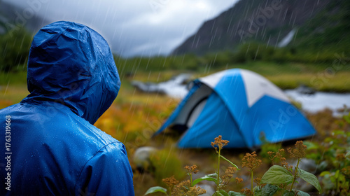 Wallpaper Mural Defocused camper in rain jacket with sharp focused vibrant blue tent on wet meadow beside mountain river, with copy space Torontodigital.ca